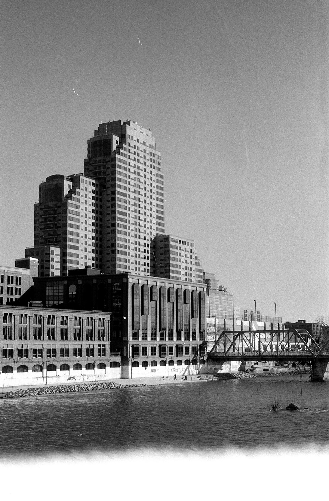 black and white photo of a sunlit, tall building downtown grand rapids, shown from across the grand river and the sky is clear.