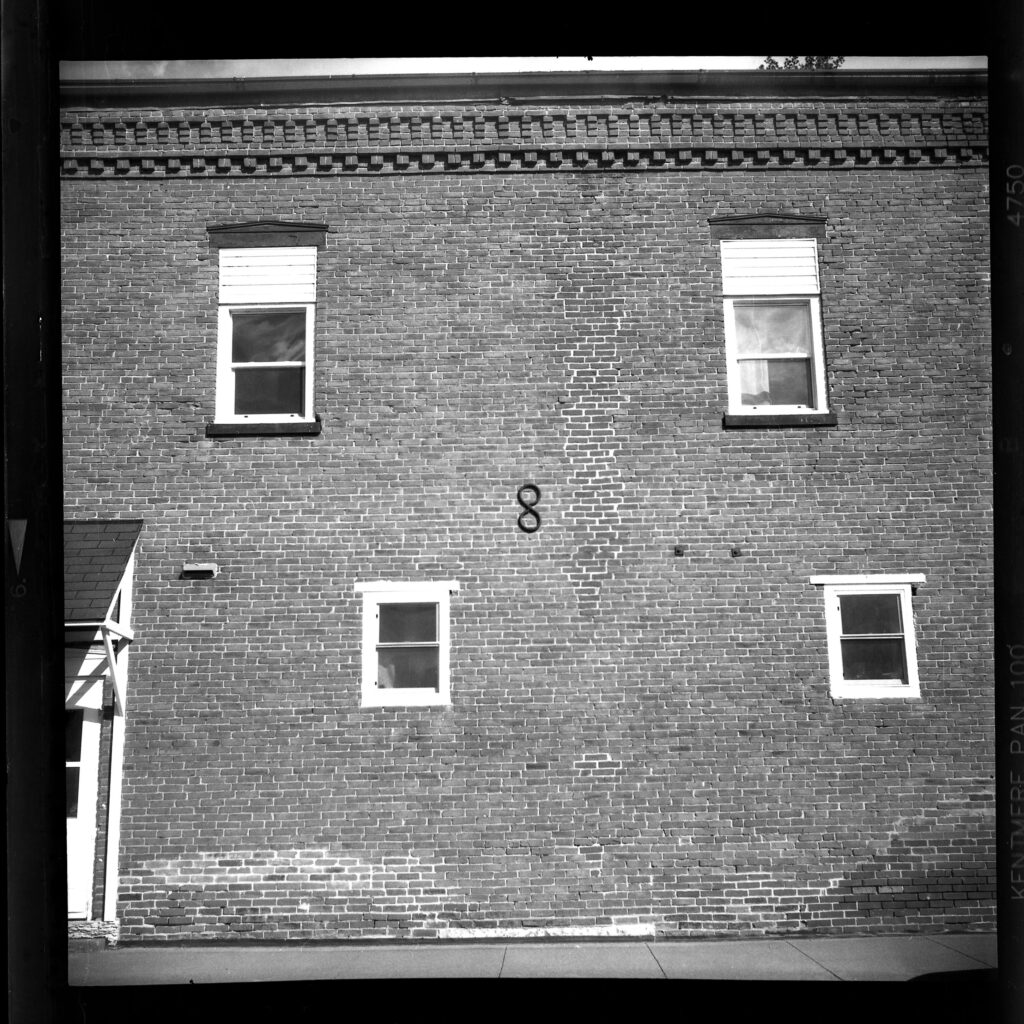 black and white photo of a brick building with 4 windows and a figure 8 in the center of the frame