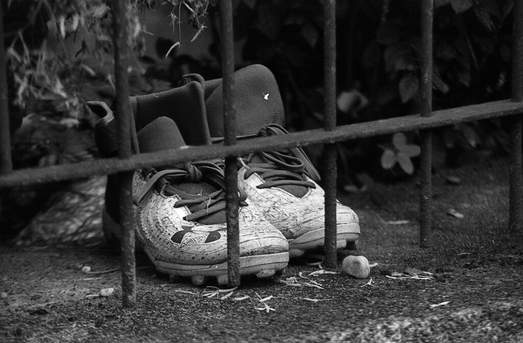 black and white photo of old cleats behind an iron fence near a garden
